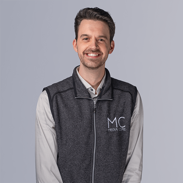 young man wearing vest smiling at camera on plain background